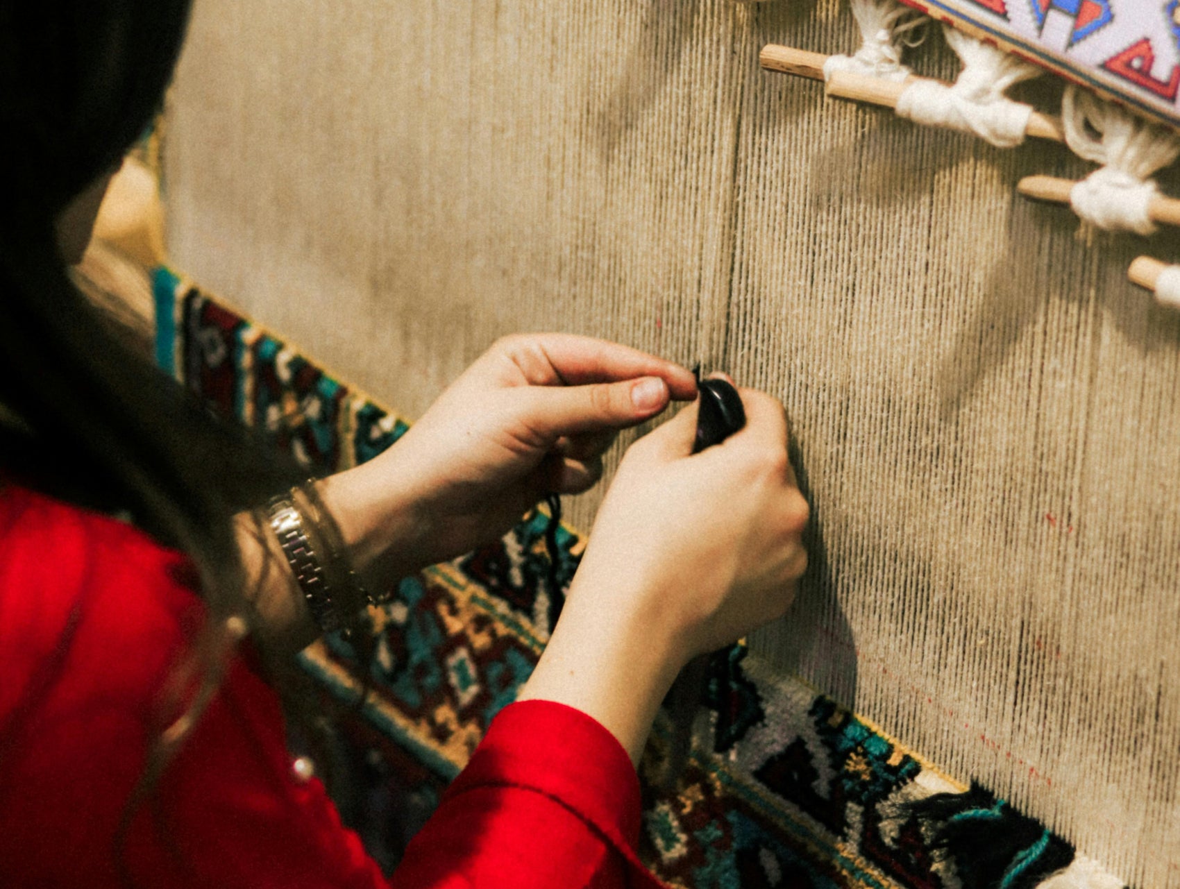 Person weaving on a loom with colorful threads and a wooden frame.